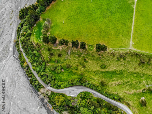 An aerial image of a rural road going between green paddock and an edge of a river on the South Island of New Zealand