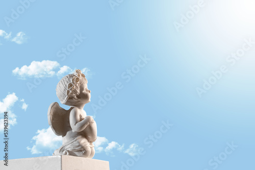 Canvastavla Figurine of an angel Cupid on the podium with a heart on a blu sky with clouds