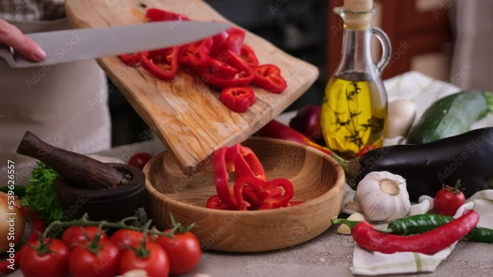 Woman pouring sliced fresh red pepper into ceramic bowl Woman pouring sliced fresh red pepper into ceramic bowl