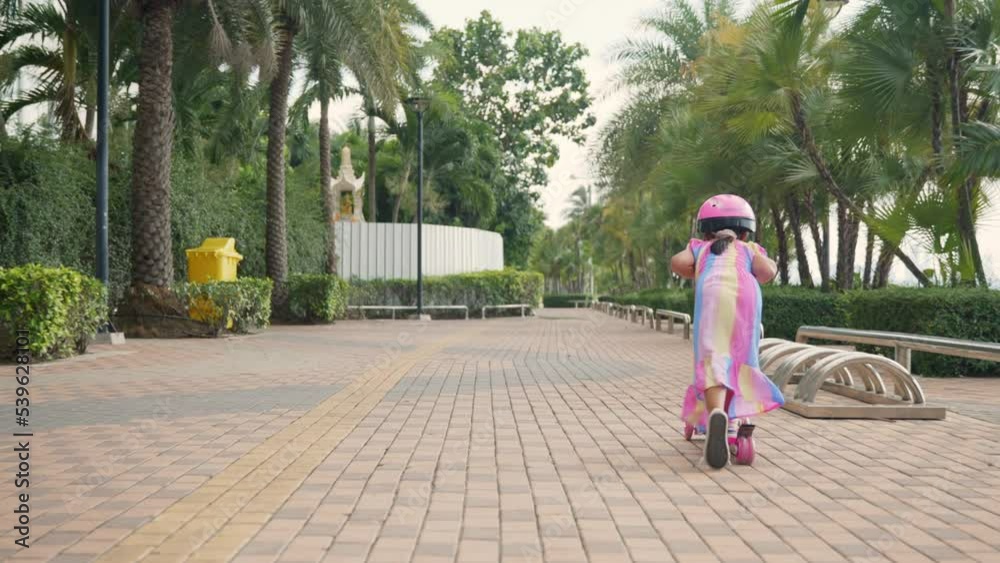 Little girl riding scooter, Safe helmet for child, Outdoor activity for children on safe residential street, Happy Asian kid preschool ride scooter or kick board on road in park outdoors on summer day