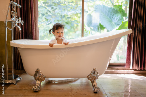 Asian cute little girl in a bathrobe having fun in a bathtub.