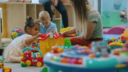 Multiracial group of little children playing with various colorful toys with their daycare teacher. Nursery playtime. Horizontal indoor shot. High quality 4k footage