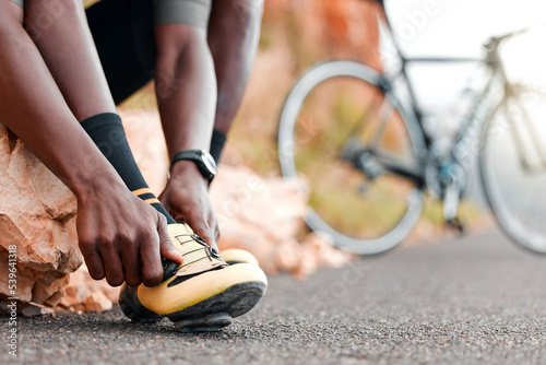 Fitness, ready and man with cycling shoes by his bicycle starting his workout, cardio exercise and training journey. Sports, healthy and African athlete biker wearing cleats for a road adventure photo