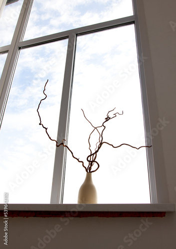 Minimalist composition with dry branches in a white ceramic vase on the background of a windowsill. © Prikhodko
