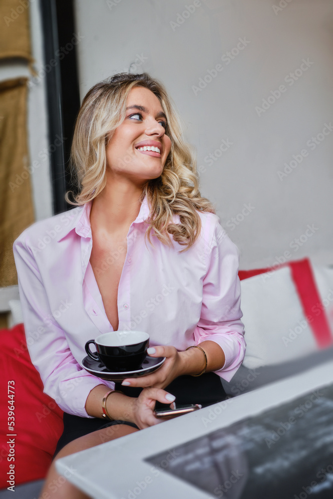 Gorgeous young blonde woman drinking coffee, holding a mug, sipping coffee in a coffee shop Gorgeous young blonde woman drinking coffee, holding a mug, sipping coffee in a coffee shop