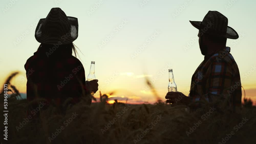 Silhouette friends farmers in straw hats in wheat field clink bottles and drink natural produced beer. Rest on leisure activity on outdoor nature landscape on sunset. Alcohol product. Countryside. Silhouette friends farmers in straw hats in wheat field clink bottles and drink natural produced beer. Rest on leisure activity on outdoor nature landscape on sunset. Alcohol product. Countryside.