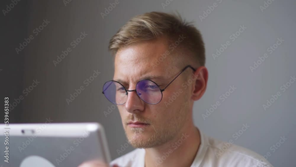 A man with glasses is watching a tablet at home. A man with glasses is watching a tablet at home.