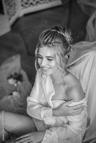 Young beautiful bride with wedding hairdo and makeup in the morning wearing a white silk negligee in the bedroom. wedding morning © capable97