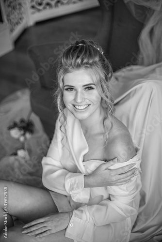 Young beautiful bride with wedding hairdo and makeup in the morning wearing a white silk negligee in the bedroom. wedding morning © capable97