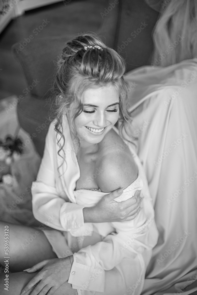 Young beautiful bride with wedding hairdo and makeup in the morning wearing a white silk negligee in the bedroom. wedding morning Young beautiful bride with wedding hairdo and makeup in the morning wearing a white silk negligee in the bedroom. wedding morning