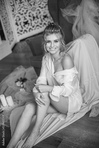Young beautiful bride with wedding hairdo and makeup in the morning wearing a white silk negligee in the bedroom. wedding morning