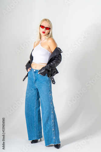 Sexy young blonde woman in a leather jacket and jeans posing on a white background