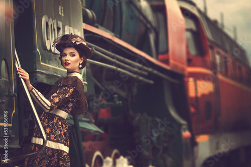 Beautiful girl in a historical retro dress on a background of an old steam locomotive, steampunk, at the railway station.
