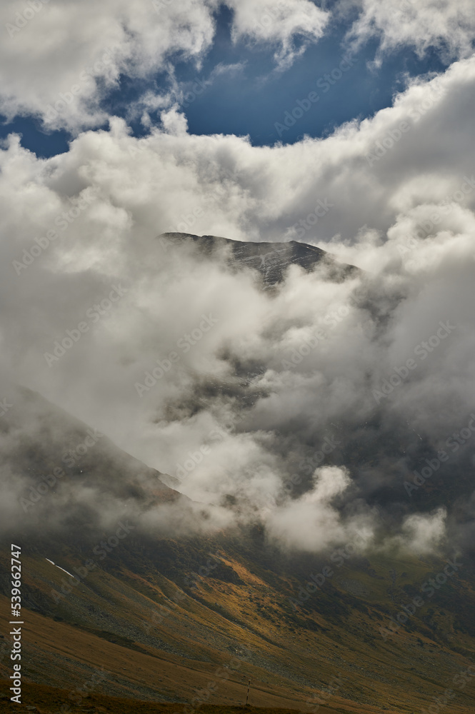 Beautiful view over a glacial valley partially covered by clouds, up in the mountains
