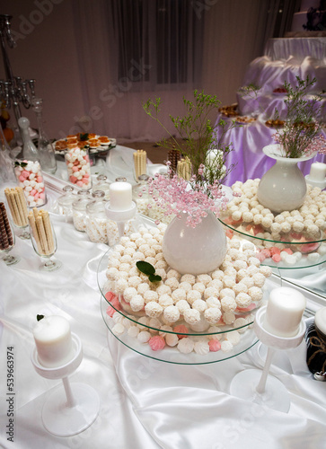 An appetizing candy bar for holiday guests stands on a table with a white tablecloth, with sweets, candles and various utensils, in the banquet room.