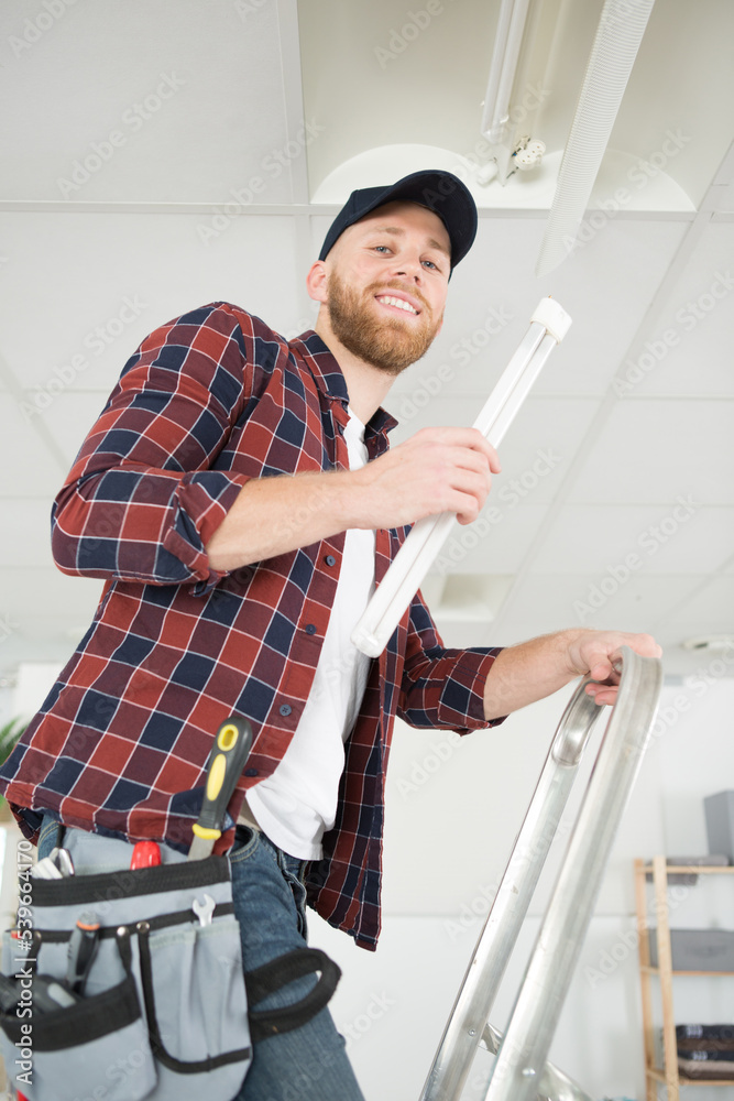 happy electrician man worker installing ceiling fluorescent lamp