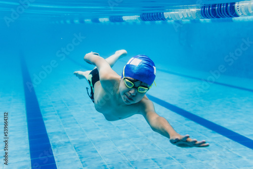 Obraz na płótnie latin child boy swimmer wearing cap and goggles in a swimming underwater trainin