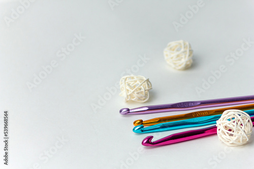 Multicolored crochet hooks of different diameters on a white background with white rattan balls. On a horizontal background. Suitable for hobby, handmade, craft and home leisure sites.