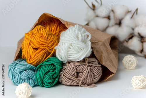 Multicolored threads in a kraft bag on a white background with a cotton ball and white rattan balls. Horizontal format. For handmade, hobby and craft.