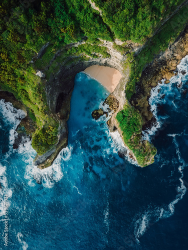 Rocks, little beach and blue ocean with waves in Bali. Aerial view.