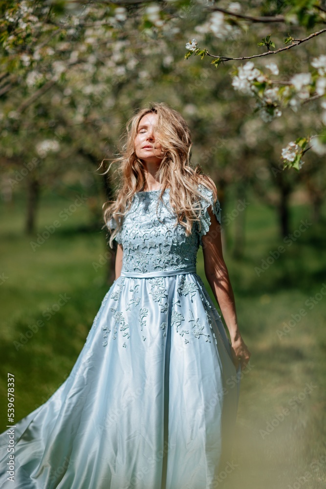 Portrait of a blonde in the park. Beautiful woman with long blond hair in a blue dress.