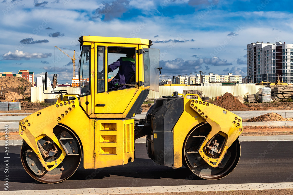 Fotka „Vibratory road roller lays asphalt on a new road under construction. Closeup of the work