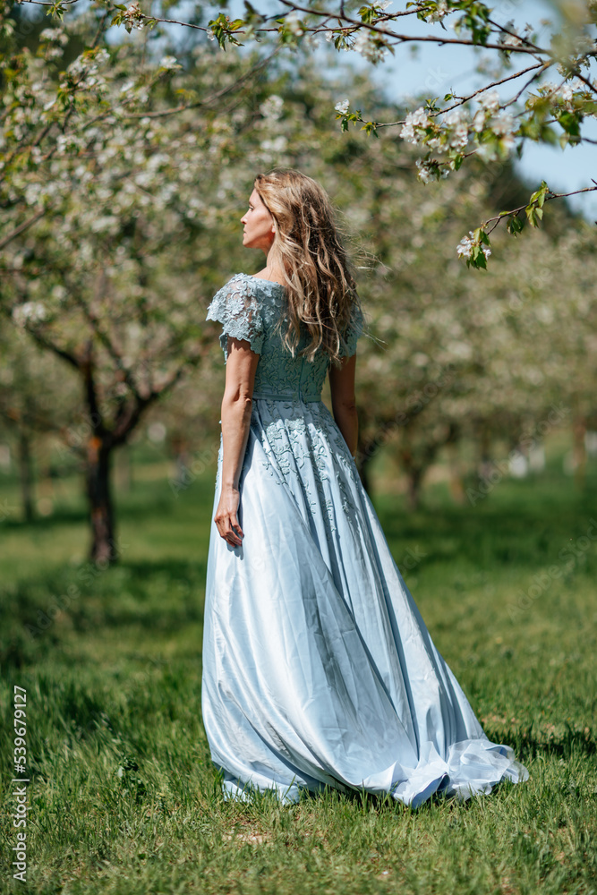 Portrait of a blonde in the park. Beautiful woman with long blond hair in a blue dress.