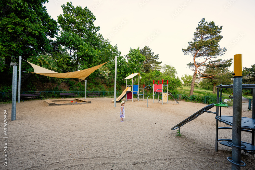 Baby girl in children's playground toy set in public park.