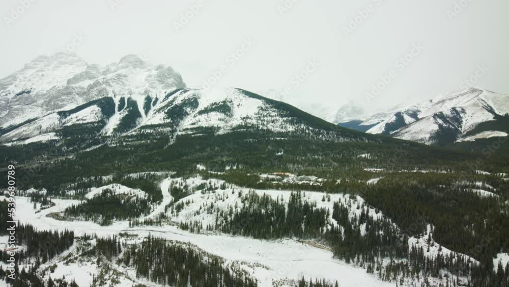 Low altitude helicopter shot of the Rocky Mountains valley in snow and with forest Low altitude helicopter shot of the Rocky Mountains valley in snow and with forest
