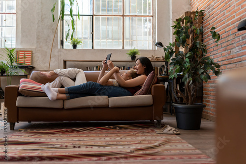 Lesbian couple lying on a sofa and using a tablet