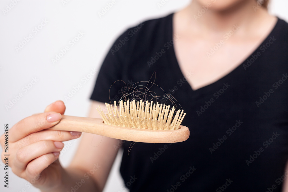 Naklejka premium Unrecognizable woman with hair loss problem holds hairbrush.