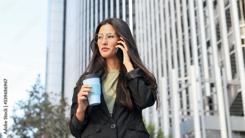 Latin business woman with glasses talking on the cell phone in a business area. Latin business woman with glasses talking on the cell phone in a business area.