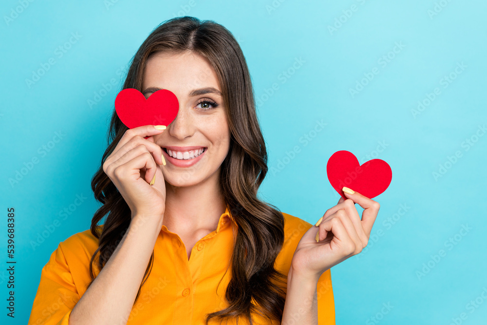 Photo of pretty positive person hands hold little red paper hearts cover one eye isolated on blue color background Photo of pretty positive person hands hold little red paper hearts cover one eye isolated on blue color background
