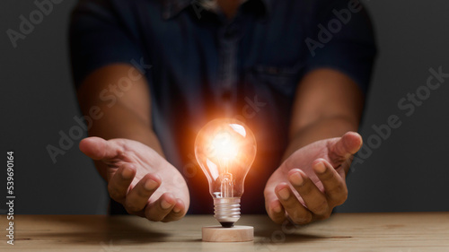 man protecting a light bulb shining orange illuminate for Creative new idea, Innovation, brainstorming, inspiration and solution concepts.