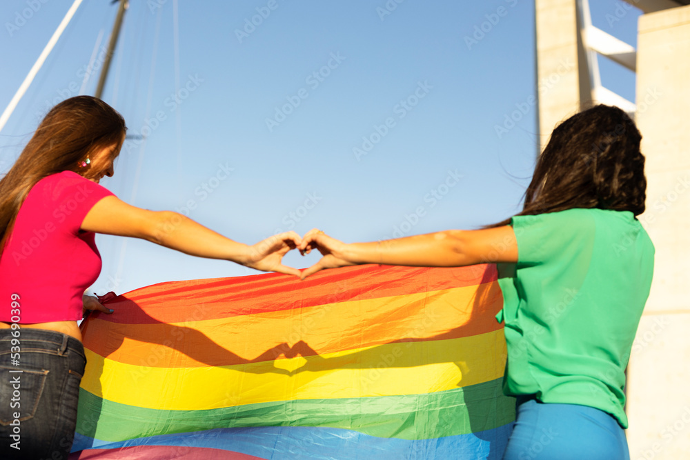 Happy couple of lesbian ladies making a heart sign with their hands.
