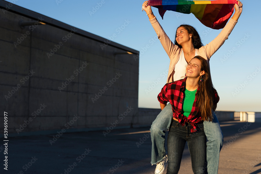 Happy lesbian young couple embraces and holds a rainbow flag. LGBT community