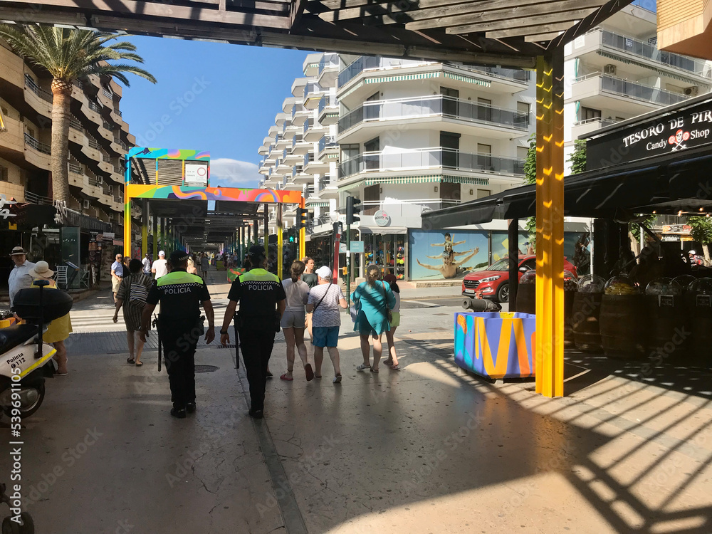 Salou, Spain, June 2019 - A group of people walking down a street next to a train station