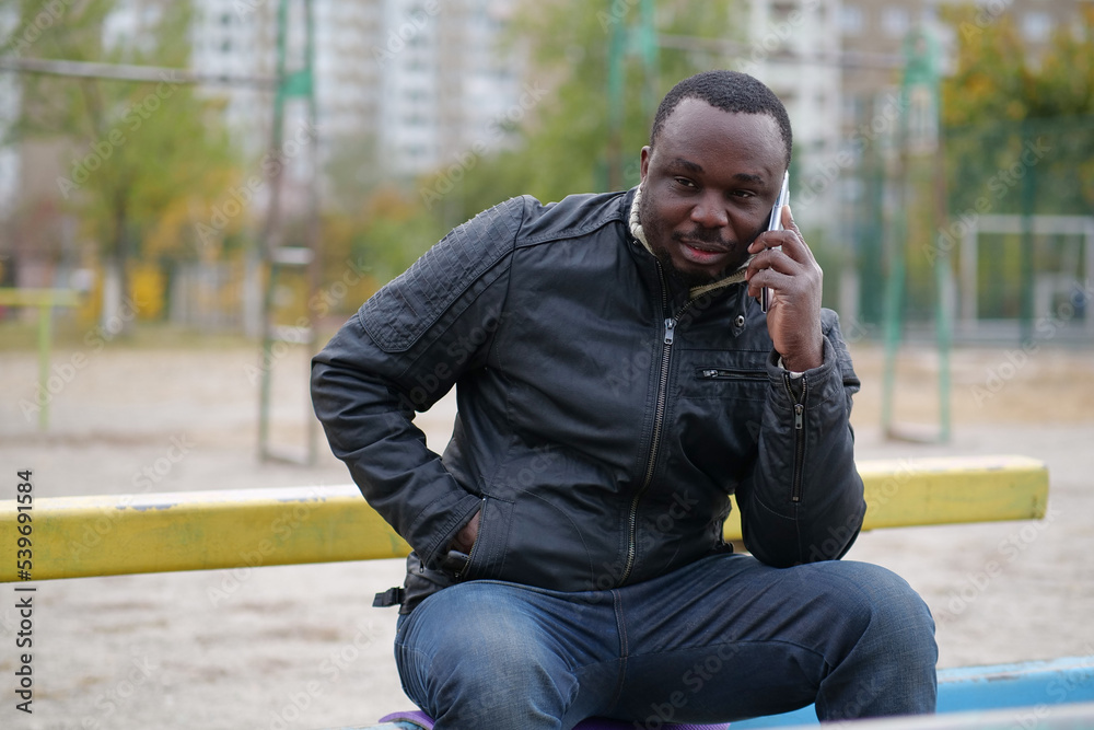 African american man sits at sport ground and speaks on smartphone African american man sits at sport ground and speaks on smartphone
