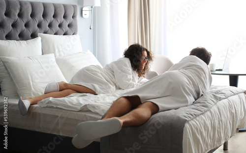 Happy couple in white bathrobe on a bed in a hotel. Morning in the hotel room.