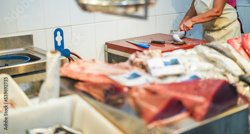 Fish monger preparing fish inside seafood market - Soft focus on woman knife cutting fish