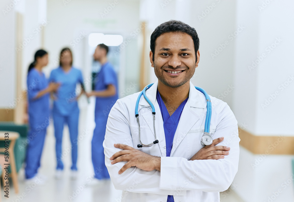 Portrait of experienced doctor from India with crossed arms and stethoscope standing in hallway of modern hospital. Medical profession Portrait of experienced doctor from India with crossed arms and stethoscope standing in hallway of modern hospital. Medical profession