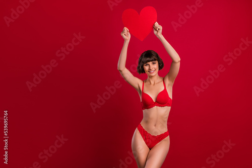 Portrait of attractive cheerful fit nude girl holding in hands heart sign 14 February isolated over bright red color background