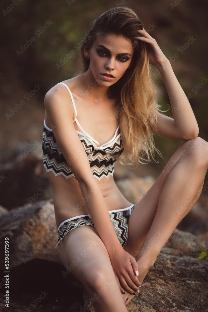 Fototapeta premium Young girl in bikini on the ocean shore. Stone background. Portrait of a Caucasian girl with European facial features.