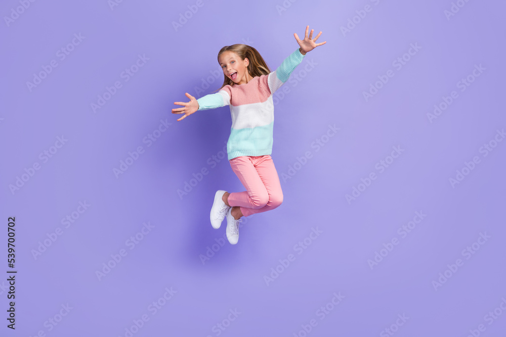 Full length photo of shiny friendly little lady dressed sweatshirt jumping high open hands isolated purple color background