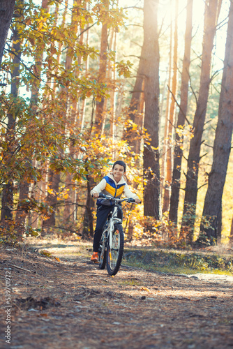 Happy kid boy having fun in autumn forest with a bicycle on beautiful fall day.