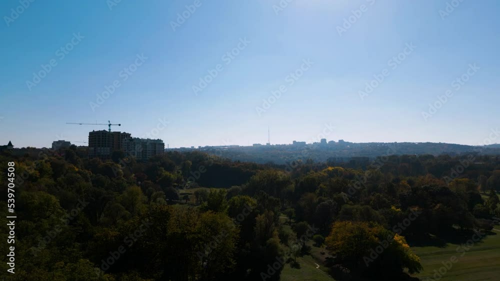 Ascending aerial drone flight over the panorama of Chisinau with construction of residential buildings on the left side, many trees forest in autumn and blue sky without clouds - bird view 2022 Ascending aerial drone flight over the panorama of Chisinau with construction of residential buildings on the left side, many trees forest in autumn and blue sky without clouds - bird view 2022