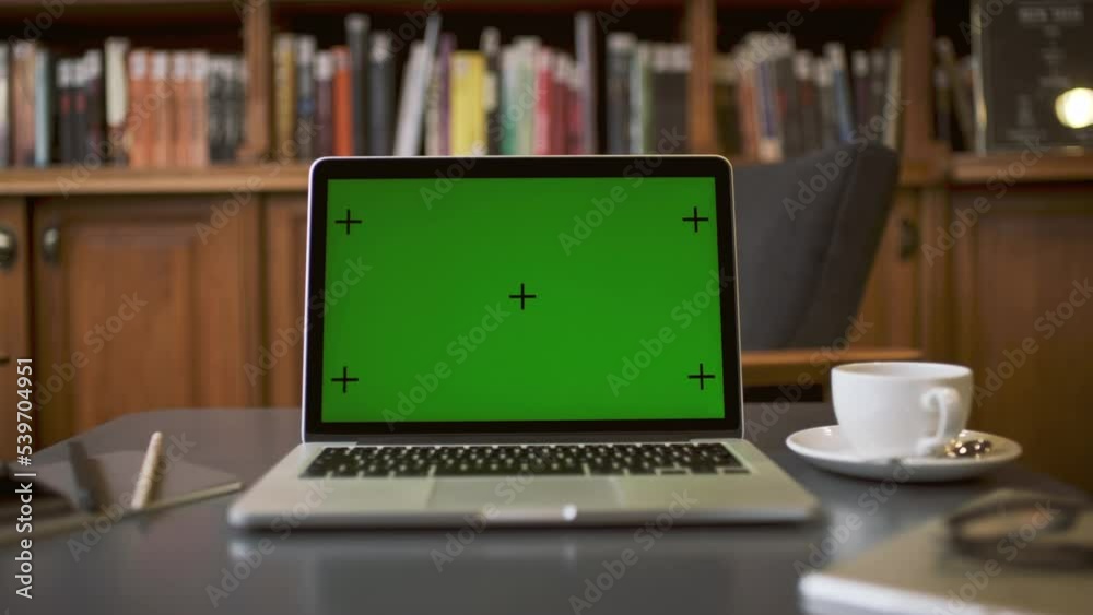 Close up footage of silver macBook pro laptop computer screen display with green screen which is good for mock ups. Laptop is placed on the table with a library or book store background.