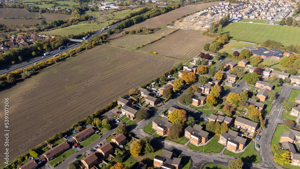Aerial drone photo of the British town of Wakefield in West Yorkshire, England showing typical British UK housing estates and roads near a farmers field and the motorway, filmed in the autumn time.