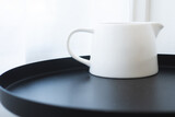 White measuring cup for fresh milk, steamed milk and poured into coffee, placed on a black table.