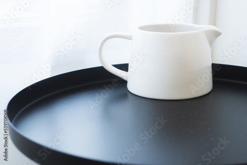 White measuring cup for fresh milk, steamed milk and poured into coffee, placed on a black table.